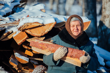 Portrait of a Russian grandmother, in the village in winter, preparing firewood, in Siberiaの写真素材