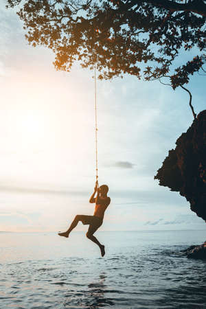 Silhouette of a guy on a swing against the sunsetの写真素材