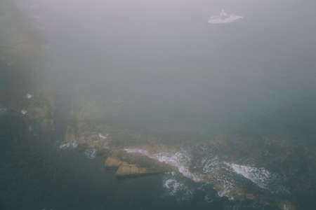 Ocean waves and coastal sea fog around the rocks, cloudy weather, storm