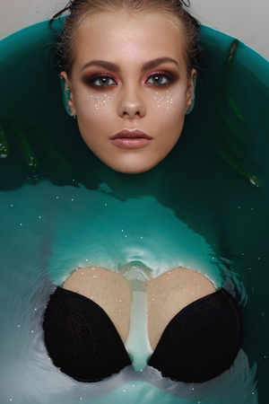 Beautiful Fashion model girl taking bath, spa and skin care concept. Beauty young Woman with bright makeup and Christmas tree branch relaxing in bath.の写真素材