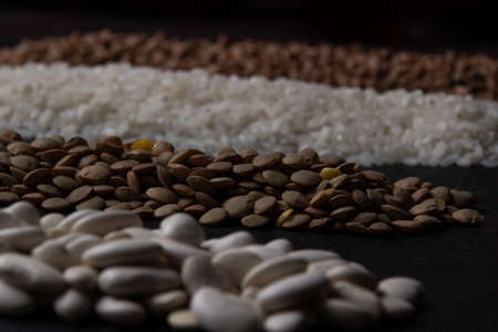 Flat lay composition with different types of grains and cereals on black background. Assortment of...
