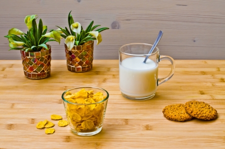 Breakfast with milk, corn flakes and cookies on a wooden table with little flowersの写真素材