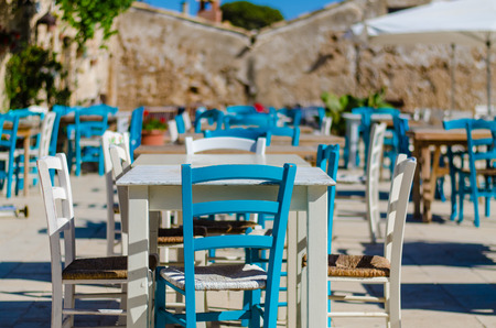 Typical mediterranean outdoor restaurants with blue and white chairs and white tablesの写真素材
