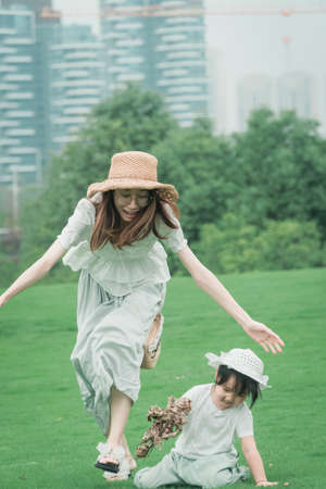 Chinese-style parent-child outdoor warm interaction, mother takes her daughter to play happily on the outdoor grass, daughter is innocent and splendid running freelyの写真素材