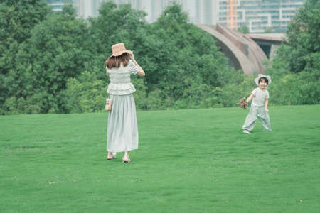Chinese-style parent-child outdoor warm interaction, mother takes her daughter to play happily on the outdoor grass, daughter is innocent and splendid running freelyの写真素材