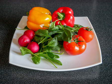 Fresh green vegetable salad with radish, tomatoes, color peppers on the white plateの写真素材