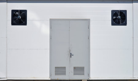 Gray metal door and two fans on white wallの写真素材