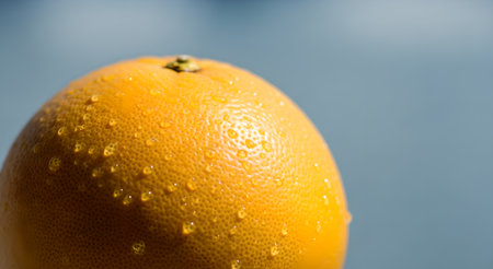 A close-up shot captures a vibrant grapefruit adorned with glistening water droplets. Its textured surface and refreshing appearance suggest a healthy and juicy treat, perfect for a sunny day.の素材