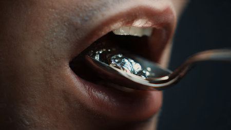 Close-up of a person putting liquid metal into their mouth with a spoon. Dark, moody concept.の素材
