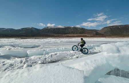 Fatbike (also called fat bike or fat-tire bike) - Cycling on large wheels. Extreme girl riding a bike on snow melted ice. The Lake Baikal.の写真素材