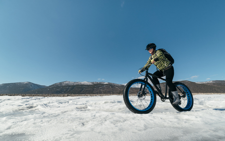 Fatbike (also called fat bike or fat-tire bike) - Cycling on large wheels. Extreme girl riding a bike on snow melted ice. The Lake Baikal.の写真素材