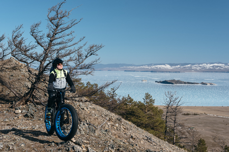 Fatbike (also called fat bike or fat-tire bike) - Cycling on large wheels. Teen riding a bike on a hill in the mountains. Against the background is Lake Baikal. The height of a hundred meters above sea level.の写真素材