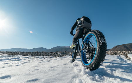 Fatbike (also called fat bike or fat-tire bike) - Cycling on large wheels. Teen rides a bicycle through the snow mountains in the background.