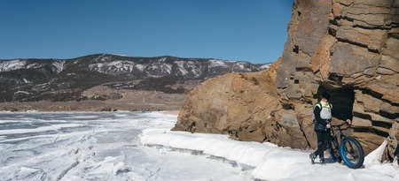 Fatbike also called fat bike or fat-tire bike - Cycling on large wheels. Traveller athlete standing on the ice of Lake Baikal, near frozen around the island. With views of the mountains and the endless ice.の写真素材