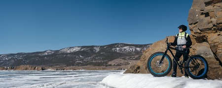 Fatbike also called fat bike or fat-tire bike - Cycling on large wheels. Traveller athlete standing on the ice of Lake Baikal, near frozen around the island. With views of the mountains and the endless ice.の写真素材