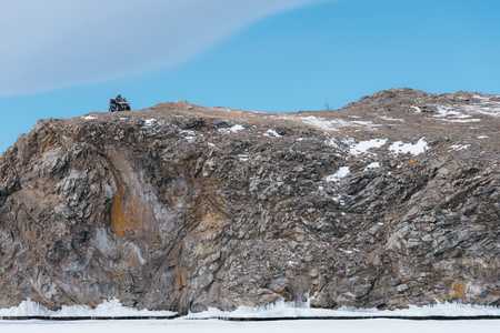 Quad bike in winter on a rock. Beautiful minimalistic landscape. Rocky high bank with a cliff. The ATV stopped and laid the route.の写真素材