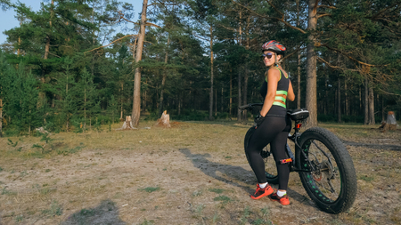 Fat bike also called fatbike or fat-tire bike in summer riding in the forest. Beautiful girl and her bicycle in the forest. She rolls her bike and poses to the operator.の写真素材