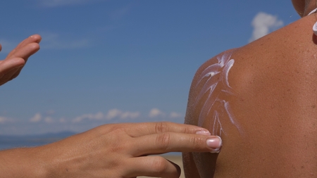 Apply sunscreen to body. A man is applying sunscreen to his woman.