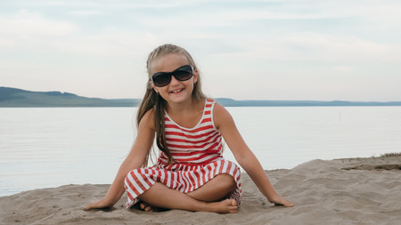 One beautiful teenage girl with brown hair outside on a beautiful summer day. The child is sitting on the beach. The sun was gone in the sunset. The kid is genuinely smiling and laughing.の写真素材