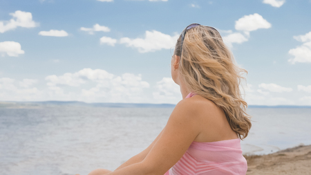 Beautiful woman is sitting on the beach. Joyful woman looks at the sea.の写真素材