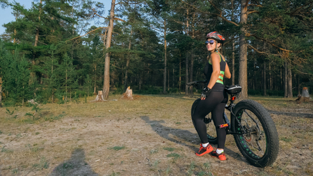 Fat bike also called fatbike or fat-tire bike in summer riding in the forest. Beautiful girl and her bicycle in the forest. She rolls her bike and poses to the operator.の写真素材