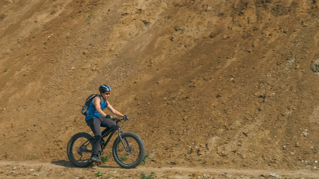 Fat bike also called fatbike or fat-tire bike in summer driving on the road. The guy rides by the hill on a sand clay path, behind him the shore by the sea.の写真素材