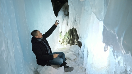 Man communicates in smartphone in an ice cave. Around the mysterious beautiful ice grotto. User...