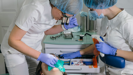 Woman at dentist clinic gets dental treatment to fill a cavity in a tooth. Dental restoration and composite material polymerization with UV light and laser. The doctor works with an assistant.の写真素材