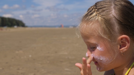 The girl apply sunscreen to face and body. The girl squeezes the sunscreen into her palm and puts it on her face.の写真素材