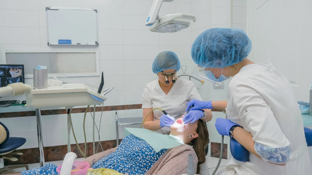 Woman at dentist clinic gets dental treatment to fill a cavity in a tooth. Dental restoration and composite material polymerization with UV light and laser. The doctor works with an assistant.の写真素材