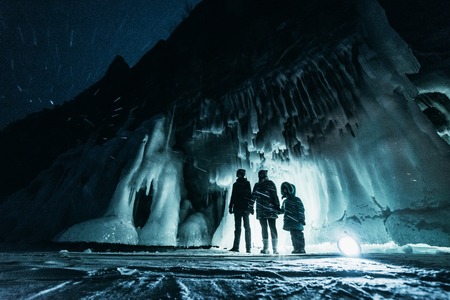 Surreal landscape with people exploring mysterious ice grotto cave. Outdoor adventure. Family...