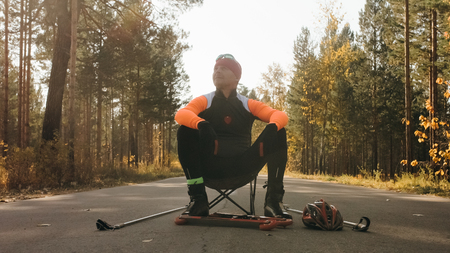 Training an athlete on the roller skaters. Biathlon ride on the roller skis with ski poles, in the helmet. Autumn workout. Roller sport. Adult man riding on skates. Athlete is getting ready to start.の写真素材