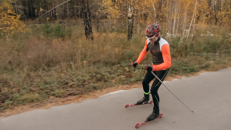 Training an athlete on the roller skaters. Biathlon ride on the roller skis with ski poles, in the helmet. Autumn workout. Roller sport. Adult man riding on skates.の写真素材