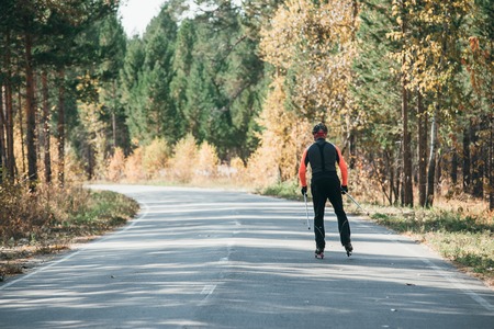 Training an athlete on the roller skaters. Biathlon ride on the roller skis with ski poles, in the helmet. Autumn workout. Roller sport. Adult man riding on skates.の写真素材