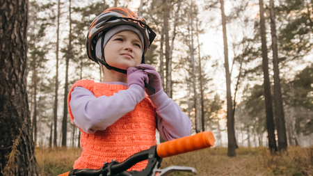 One caucasian children walk with bike in autumn park. Little girl walking black orange cycle in forest. Kid goes do bicycle sports. Biker motion ride with backpack and helmet. Mountain bike hardtail.の写真素材
