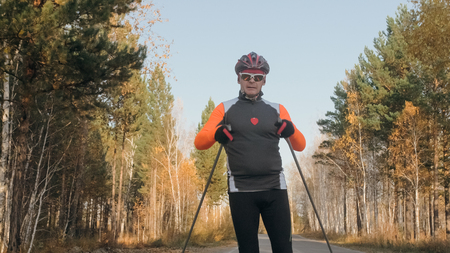 Training an athlete on the roller skaters. Biathlon ride on the roller skis with ski poles, in the helmet. Autumn workout. Roller sport. Adult man riding on skates.の写真素材