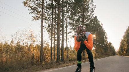 Training an athlete on the roller skaters. Biathlon ride on the roller skis with ski poles, in the helmet. Autumn workout. Roller sport. Adult man riding on skates.の写真素材
