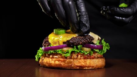 Craft burger is cooking on black background. Consist: red sauce salsa, lettuce, red onion, pickle, cheese, chilli green pepper, air bun and marbled meat beef. Not made ideal. Loving hand made.の写真素材