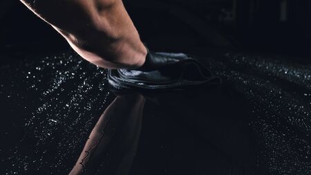 Using rag in palm of your hand, drops are removed from the car. Drop flow down the hood. Close up view of bonnet car. Process of polishing and washing auto. Hose is poured over cowl with water.の写真素材