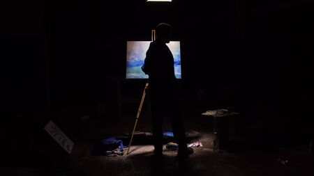 Artist copyist paint seascape with ship in ocean. Craftsman decorator draw as boat sail on blue sea with acrylic oil color. Black background. Indoor. Wide angle shot cinematic look.の写真素材