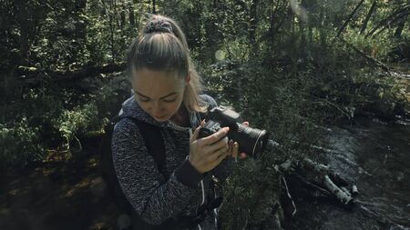 Traveler photographing scenic view in forest river. Wood bridge fallen tree. One caucasian woman...