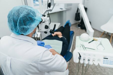 Doctor used microscope. Dentist is treating patient in modern dental office. Operation is carried...