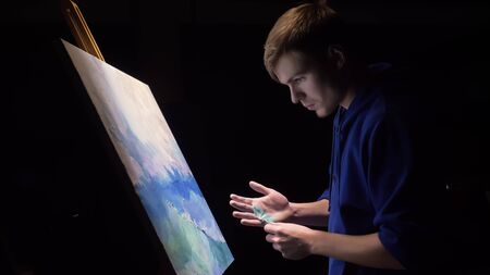 Artist copyist paint seascape with ship in ocean. Craftsman decorator draw as boat sail on blue sea with acrylic oil color. Draw finger, brush, knife palette. Canvas, easel in studio, indoor.の写真素材