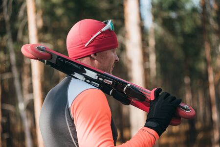 Training an athlete on the roller skaters. Biathlon ride on the roller skis with ski poles, in the helmet. Autumn workout. Roller sport. Adult man riding on skates.の写真素材