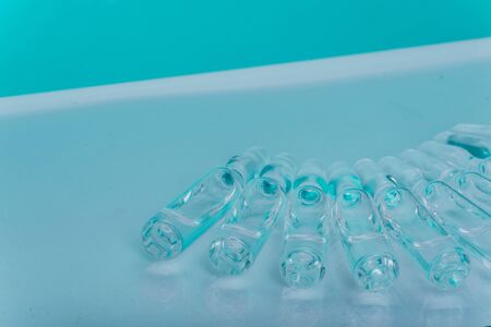 Glass medical ampoule vial for injection. Medicine is liquid sodium chloride with of aqueous solution in ampulla. Close up. Bottles ampule multicolor on background color and water. Human plasma.の写真素材