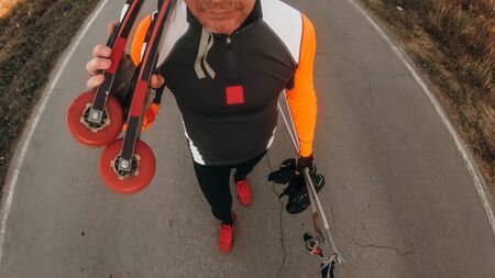 Training an athlete on the roller skaters. Pov view action cam. Biathlon ride on the roller skis with ski poles, in the helmet. Autumn workout. Roller sport. Adult man riding on skates.の写真素材