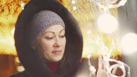 Pretty woman walking along the black fur coat. Outdoor. Girl walks on a winter night among the street lights of the city. Snow park with garlands. Beautiful sensual happy smile.の写真素材