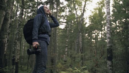 Traveler photographing scenic view in forest. One caucasian woman shooting nice magic look. Girl take photo video on dslr mirrorless camera. Professional photographer travel with backpack. Outdoor.の写真素材
