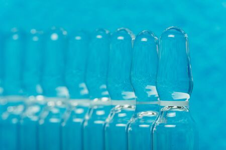 Glass medical ampoule vial for injection. Medicine is liquid sodium chloride with of aqueous solution in ampulla. Close up. Bottles ampule multicolor on background color and water. Human plasma.の写真素材