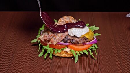 Craft burger is cooking on black background. Consist: sauce, arugula, tomato, red onion, bacon, red currant sauce, ricotta cottage fresh cheese, air bun and marble meat beef. Not made ideal. Looks real, loving hand made.の写真素材